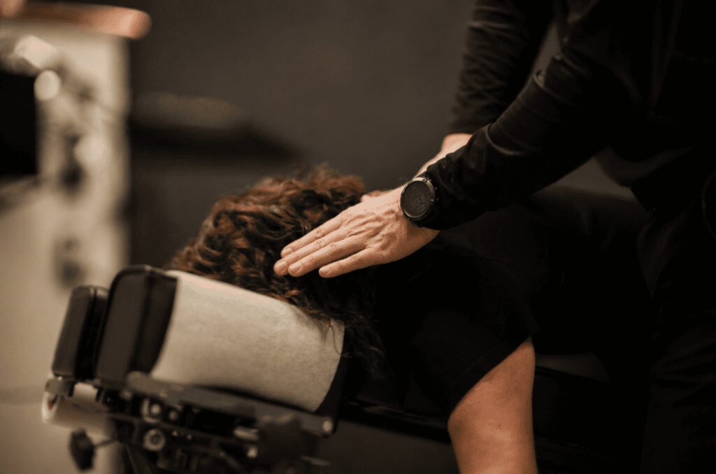 Close-up of a practitioner’s hand gently adjusting a patient lying face-down on a treatment table, with shallow depth of field and soft background blur.