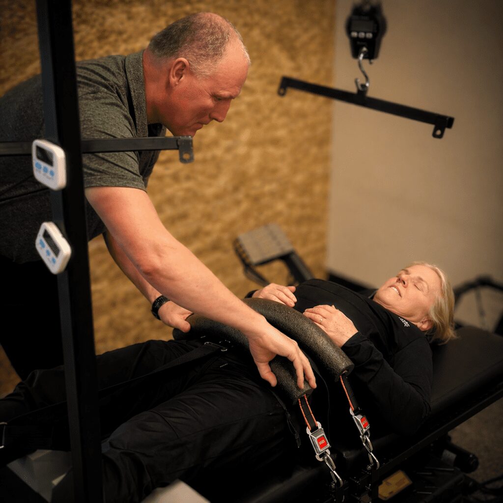 Therapist adjusting supportive straps on a patient lying on a treatment table in a softly lit clinic.