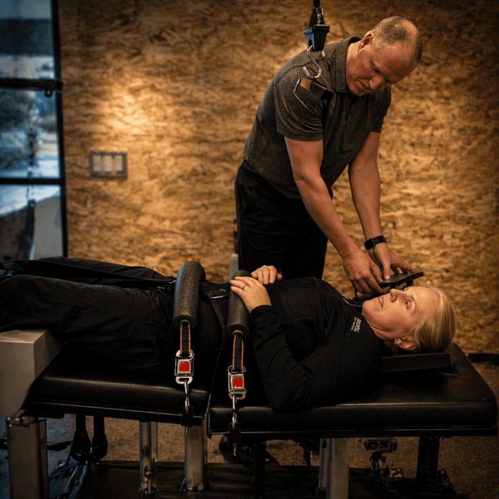 Therapist assisting a patient lying on a treatment table with traction equipment in a warm, softly lit clinic.