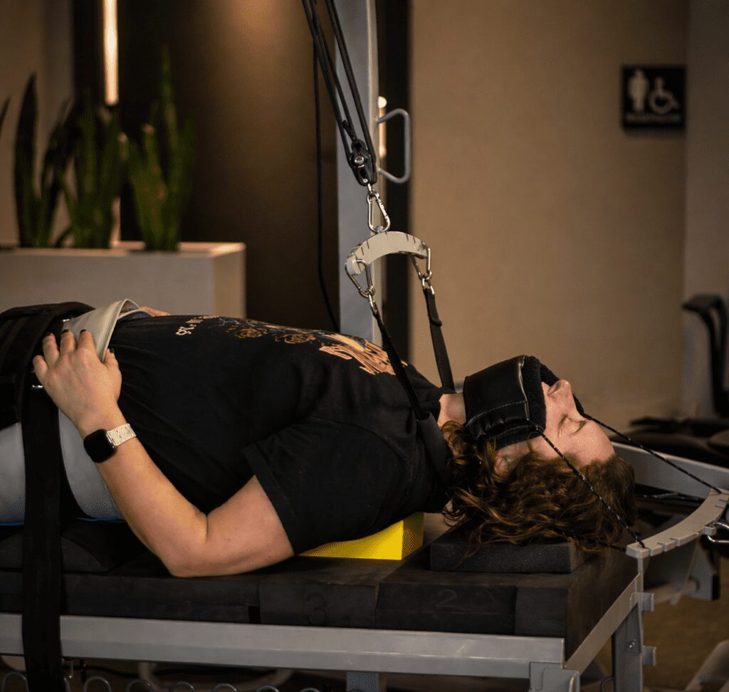 Patient lying on a treatment table undergoing neck traction therapy with harness in a softly lit clinic environment.